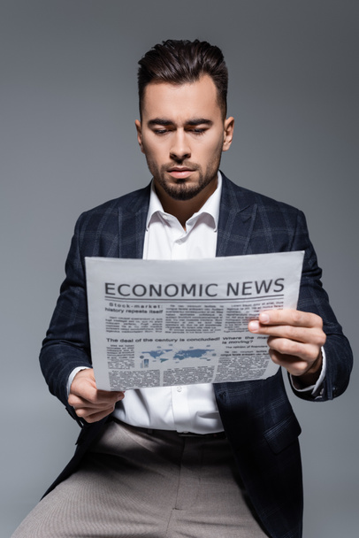 hombre de negocios barbudo en chaqueta a cuadros leyendo periódico con noticias económicas aisladas en gris - Foto, Imagen