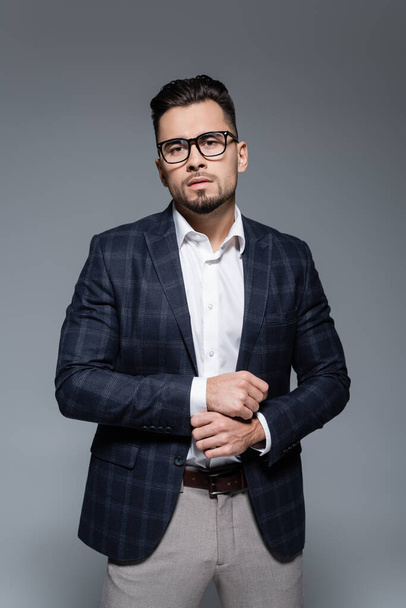 bearded businessman in blazer and glasses looking at camera isolated on grey - Фото, изображение