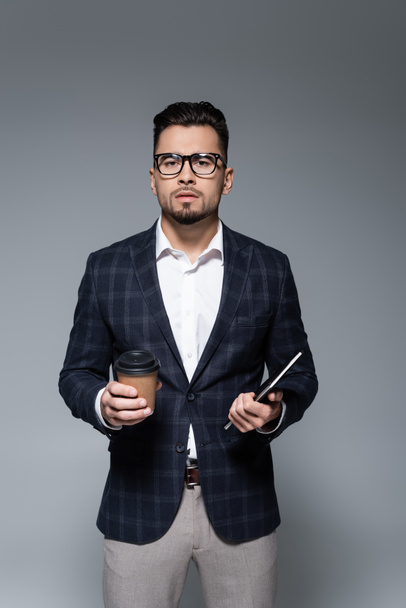 businessman in glasses and blazer holding paper cup and notebook isolated on grey - Foto, imagen