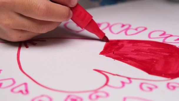 Close-up van een klein meisje dat een hart tekent en kleurt met haar gekleurde stiften. Schattig jong meisje doet huiswerk aan tafel thuis. Kunstnijverheid. - Video