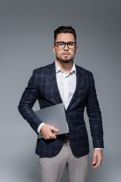 businessman in blazer and glasses holding laptop isolated on grey - Fotografie, Obrázek