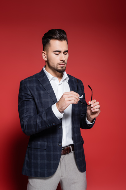 bearded businessman in checkered blazer holding glasses on red - Foto, immagini
