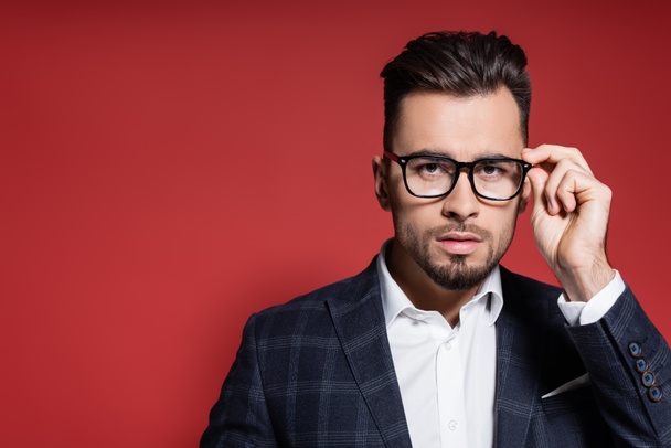 bearded businessman in plaid blazer adjusting glasses on red - Foto, immagini