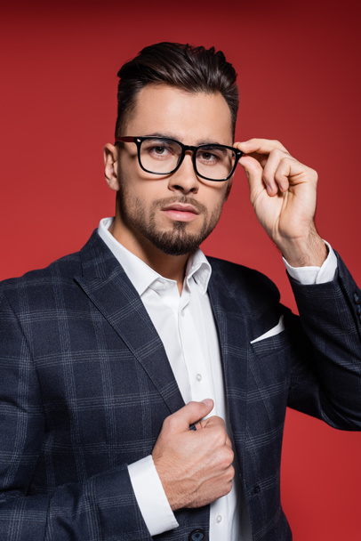 bearded businessman in checkered suit adjusting glasses on red - Fotoğraf, Görsel