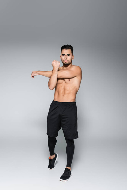 full length of young bearded and muscular sportsman warming up on grey - Foto, afbeelding