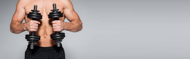 osittainen näkymä paidaton ja lihaksikas urheilija treenata käsipainot eristetty harmaa, banneri - Valokuva, kuva
