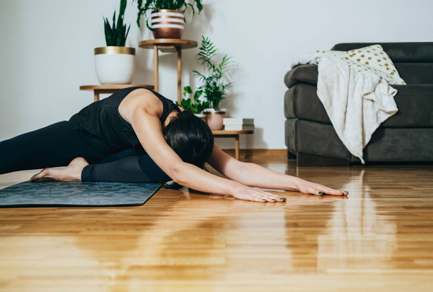 An Anonymous Woman Doing Home Work Out Training. Unrecognizable fitness woman stretching legs and arms on a gray exercise mat in the living room at home.  - Valokuva, kuva