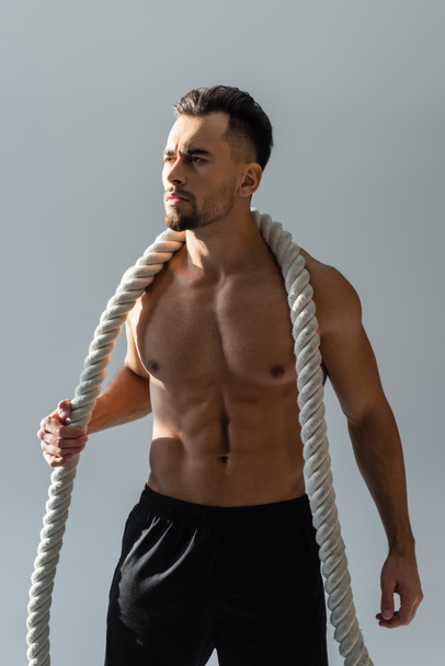 shirtless sportsman holding heavy battle ropes on shoulders looking away isolated on grey - Photo, Image