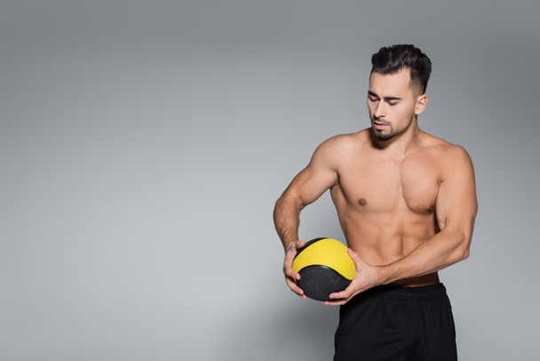 muscular and bearded sportsman looking at ball on grey - Foto, Bild
