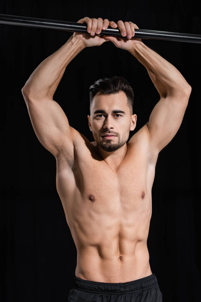 shirtless and muscular sportsman looking at camera near horizontal bar isolated on black  - Photo, Image