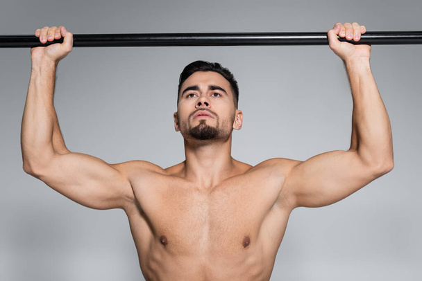 muscular young sportsman exercising on horizontal bar isolated on grey - Foto, afbeelding