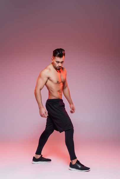 full length of shirtless sportsman posing on grey and pink  - Foto, afbeelding