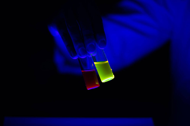 Glasfläschchen mit giftigen chemischen Proben, die eine Wissenschaftlerin in einem Labor hält - radioaktive Fluoreszenz. Ein schwarzer Hintergrund. - Foto, Bild