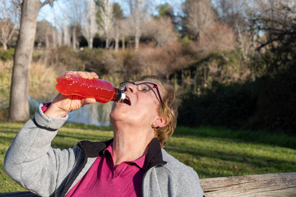  Mulher idosa bebendo uma bebida isotônica de uma garrafa de plástico - Foto, Imagem