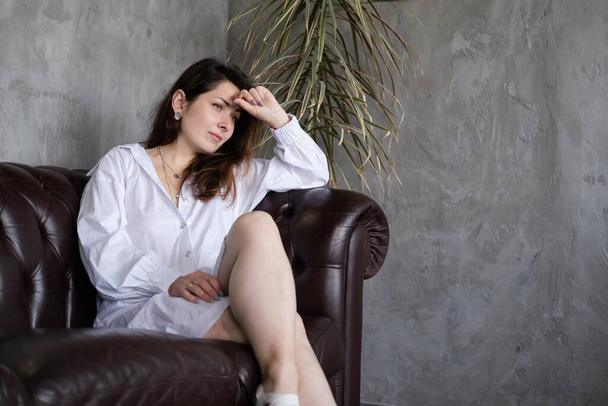 confident brunette woman in white shirt on leather couch - Photo, image