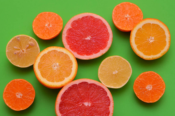 緑の背景に様々な種類の柑橘類のスライスをクローズアップ - 写真・画像