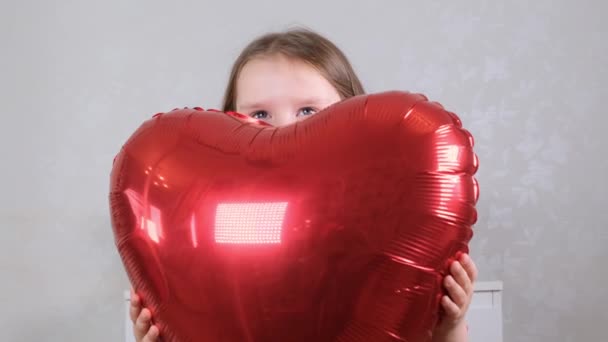 little cute girl in a red dress gently hugs red heart shaped balloons with her hands. valentines day concept - Video