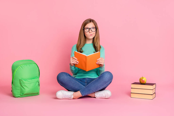 Photo of doubtful school girl dressed teal pullover reading book supplies empty space isolated pink color background - Valokuva, kuva