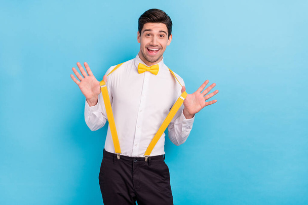 Photo of funny excited guy wear yellow suspenders white shirt rising arms smiling isolated blue color background - Photo, image