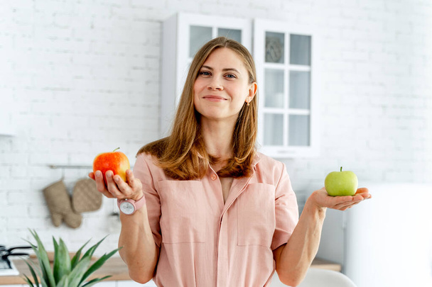 Cheerful beautiful woman looking into camera with apple. Playful pretty lady posing with healthy food. - 写真・画像