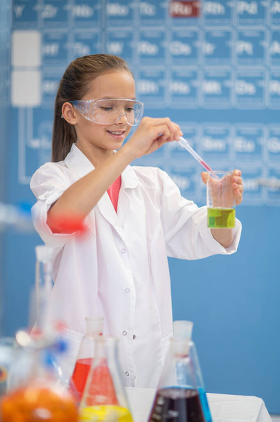 Girl with pipette over test tube standing in classroom - Photo, Image