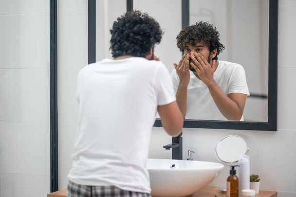 Concentrated young man examining his facial skin - Foto, afbeelding