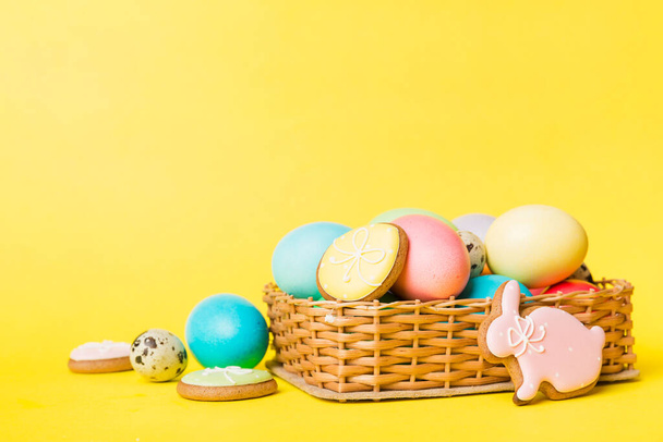カラフルなイースタークッキーバスケットに複数の色のイースターの卵色の背景に。パステルカラーイースターエッグ。コピースペース付きの休日のコンセプト. - 写真・画像