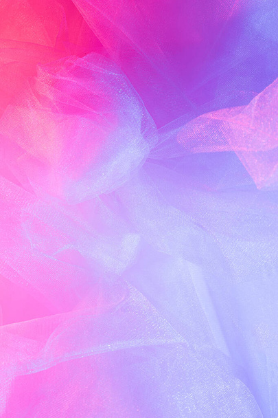 Neon fashion blog concept. Light pink tulle fabric enlightened with two colors  blue and red. Background from pink crumpled tulle. Textured background for atelier. - Photo, Image