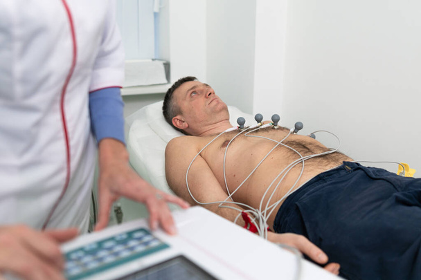 Orvosi felszerelés elektrokardiogramhoz. Az orvosok férfi betegen végeznek EKG tesztet. Diagnosztikai szívbetegség szívroham, tachycardia. Elektrokardiográfia. Kardiológus ellenőrző vizsgálat elvégzése. - Fotó, kép