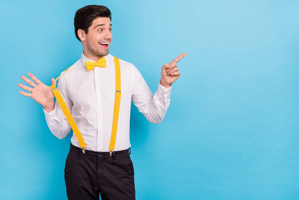 Photo of dreamy charming guy dressed white shirt yellow bowtie pointing looking empty space isolated blue color background - Foto, Imagem