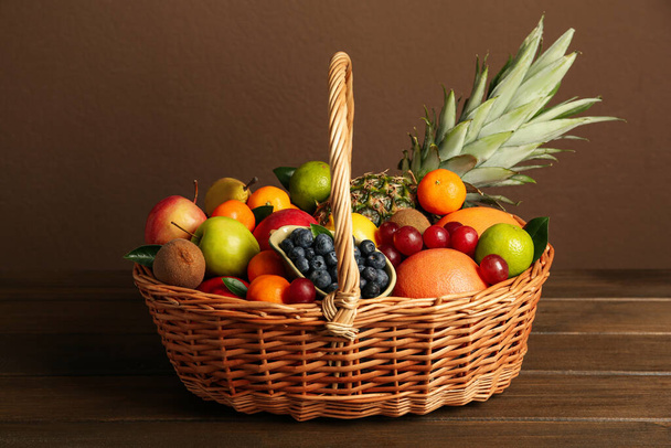 Assortment of fresh exotic fruits in wicker basket on wooden table - Фото, изображение