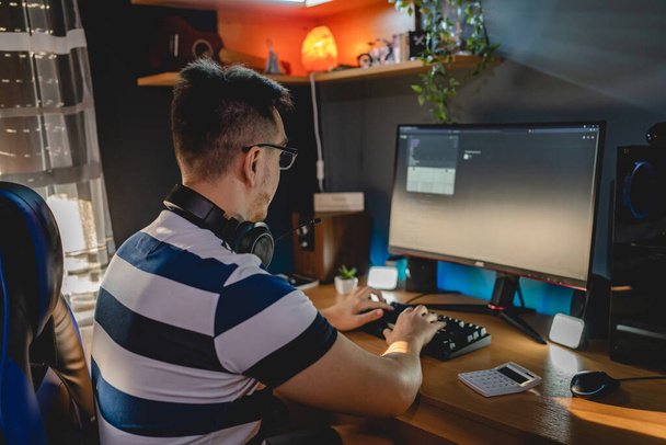 Widok z tyłu dorosłego człowieka rasy kaukaskiej siedzącego przy stole komputerowym w domu patrzącego na ekran monitora z wykresem sprawdzającym rynek kursów walut kryptowaluta i górnicze inwestycje prawdziwych ludzi - Zdjęcie, obraz
