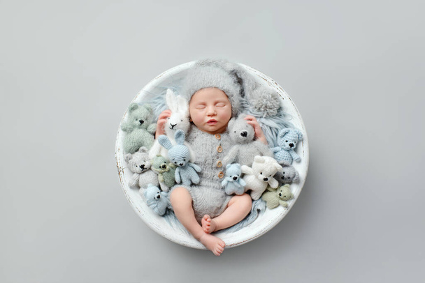 Slapen pasgeboren baby op een grijze achtergrond met speelgoed. Fotoshoot voor de pasgeborene. Een paar dagen na de geboorte. - Foto, afbeelding