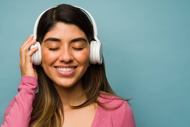 Uvolněná mladá žena pomocí bílých bezdrátových sluchátek a poslech relaxační hudby se zavřenýma očima - Fotografie, Obrázek