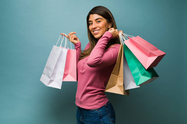 Glückliche junge Frau, die sich beim Einkaufen im Einkaufszentrum vor blauem Hintergrund gut gelaunt fühlt  - Foto, Bild