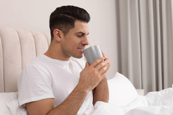 Happy man with cup of hot drink in bed at home - Photo, Image