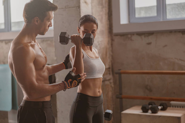 Muscular man in the gym with athletic woman performing sports exercises - Photo, Image