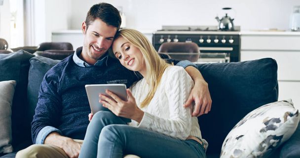 ネットを一緒にサーフィン。自宅でソファに座っている間、デジタルタブレットを使用して愛情のある若いカップルの作物のショット. - 写真・画像