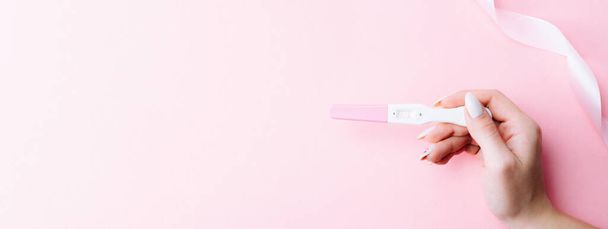 Raskaustesti onnellinen. Naiskädellä positiivinen raskaana testi silkkinauhalla vaaleanpunaisella taustalla. Lääketieteellinen terveydenhuolto gynekologinen, raskaus hedelmällisyys äitiys ihmiset käsite - Valokuva, kuva