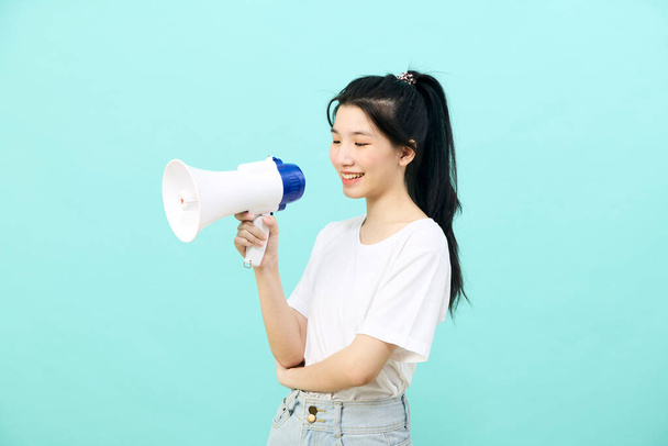 Beautiful young Asian woman holding megaphone on blue background studio - 写真・画像