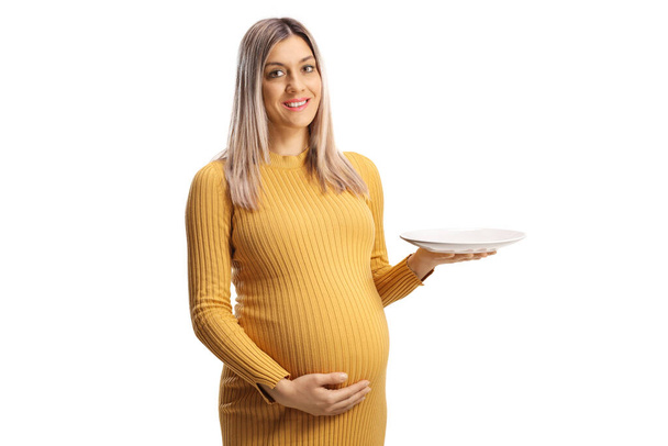 Pregnant woman holding an empty plate and smiling isolated on white background - Zdjęcie, obraz