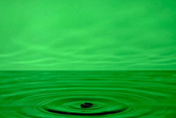 Bright green background with diverging circles from dropped drop on surface water - Foto, Bild