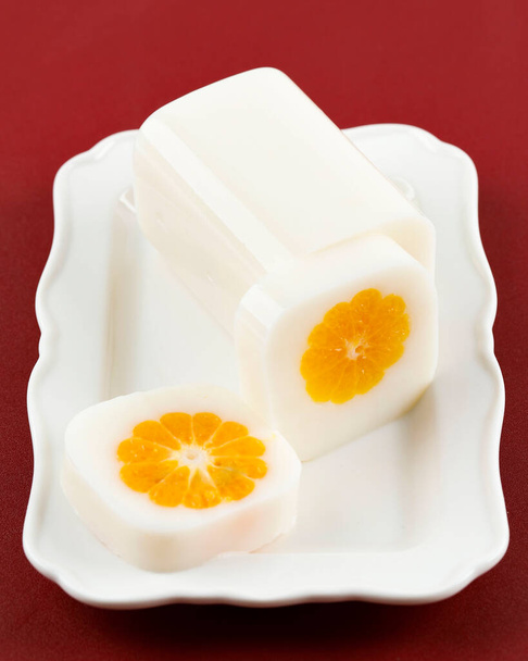 Γάλα Pudding με φρέσκο πορτοκάλι στο κέντρο, σε λευκό πιάτο, κόκκινο τραπέζι - Φωτογραφία, εικόνα