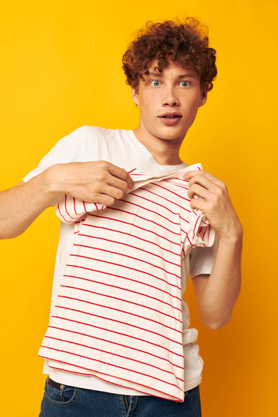 guy with red curly hair in a white t-shirt holds a striped t-shirt fashion youth style Lifestyle unaltered - Foto, Bild
