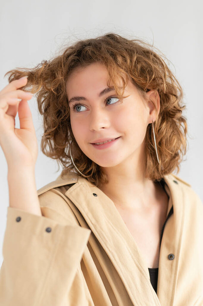 Portrait of Caucasian woman with smoothly tucked hair and natural makeup in raincoat with. woman looking at curly hair - Photo, Image
