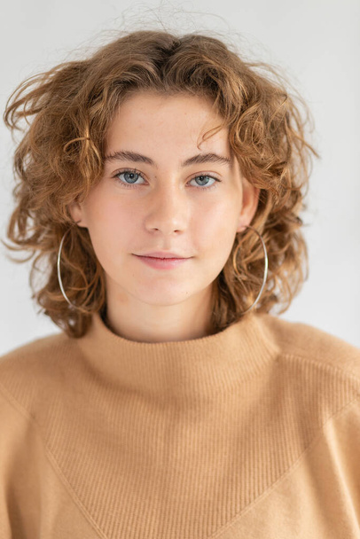 Portrait of confident attractive employee with short curly hair, wearing office blouse while smiling broadly and standing against gray background, posing for advertising purpose - 写真・画像