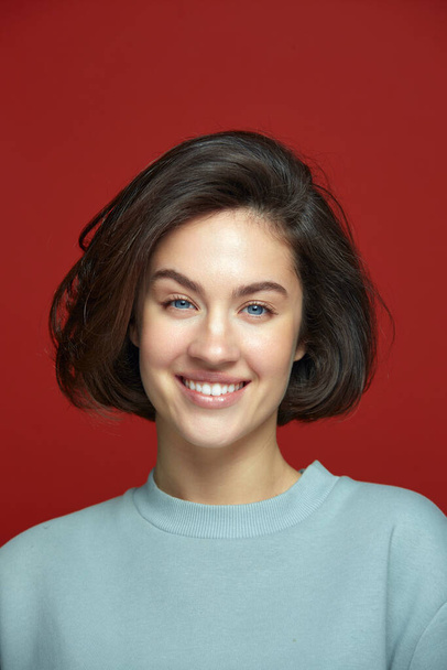 Ευτυχισμένο όμορφο νεαρό κορίτσι χαμογελώντας με τέλειο λαμπερό λευκό χαμόγελο σε κόκκινο φόντο. Οδοντιατρική κλινική, λεύκανση δοντιών διαφήμιση - Φωτογραφία, εικόνα