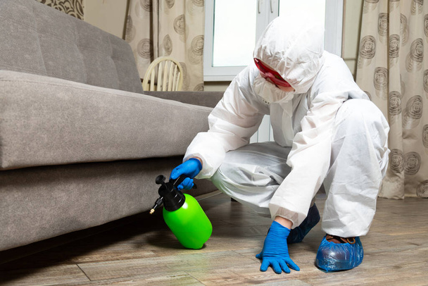 An exterminator in work clothes sprays pesticides with a spray gun. Fight against insects in apartments and houses. Disinsection of the premises - Foto, imagen