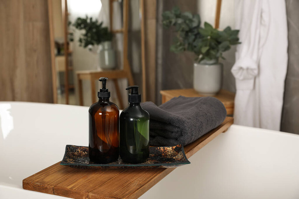 Wooden bath tray with bottles of shower gels and towel on tub indoors, space for text - Фото, зображення