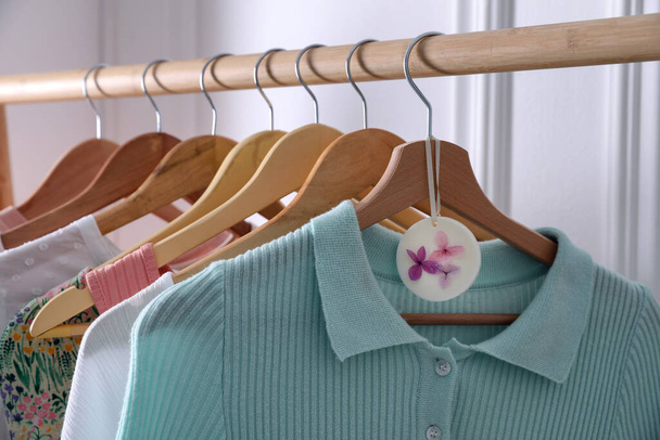 Beautiful scented wax sachet and clothes hanging on wooden rack indoors - Φωτογραφία, εικόνα